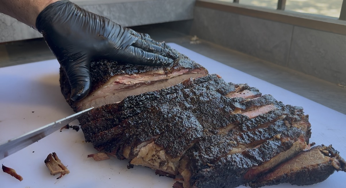Hand slicing a whole smoked brisket with dark peppery bark